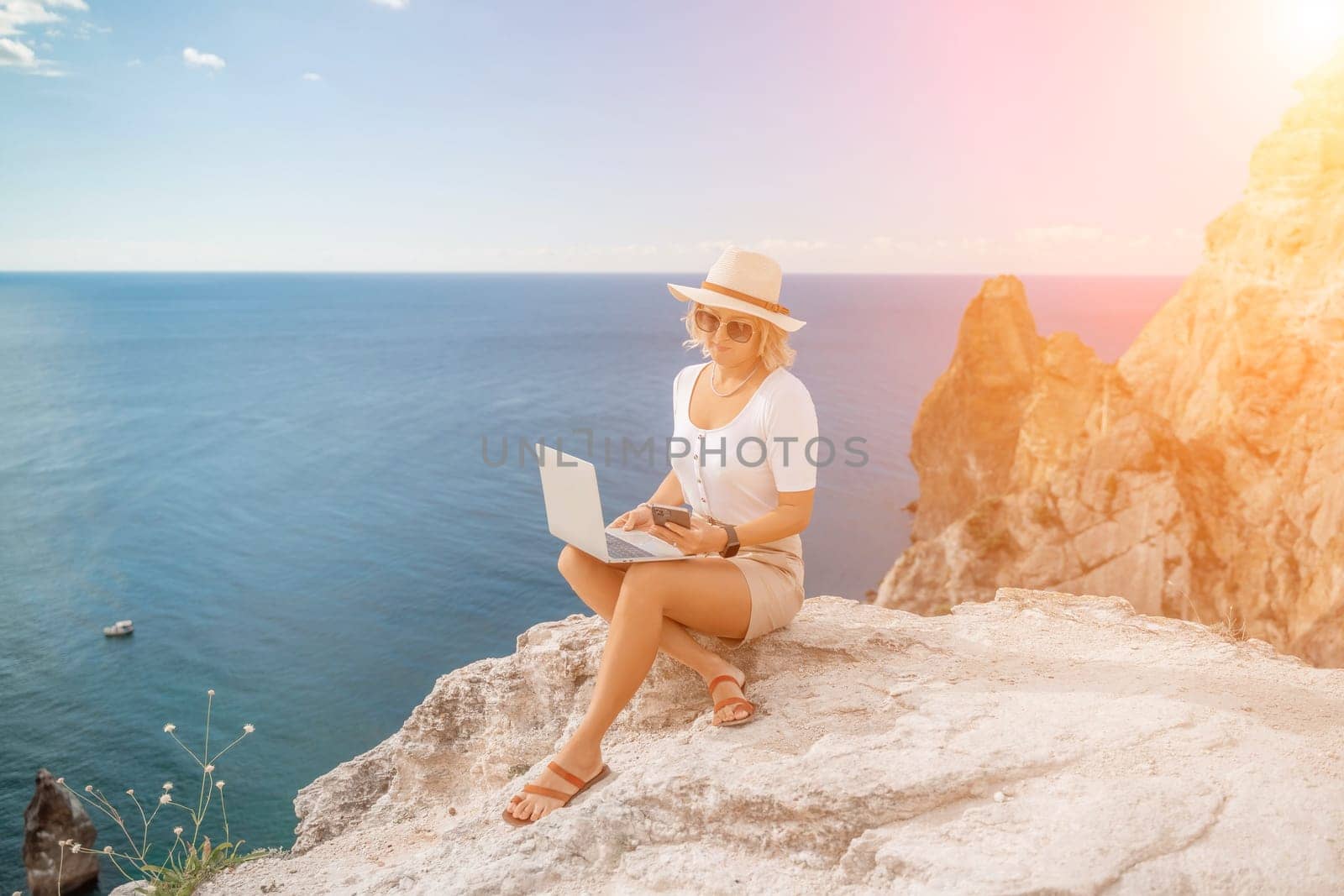 Freelance women sea working on the computer. Good looking middle aged woman typing on a laptop keyboard outdoors with a beautiful sea view. The concept of remote work. by Matiunina