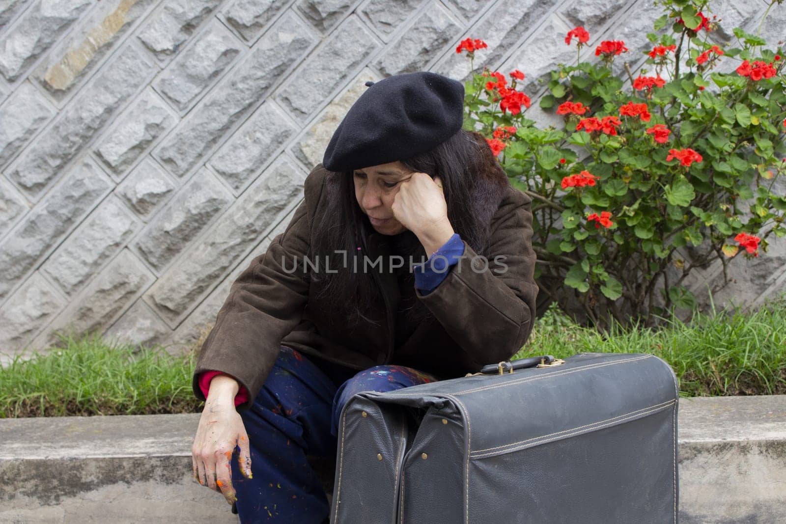 unhappy retired woman with suffering, emotional stress and depression sitting on the street next to an old gray suitcase. High quality photo