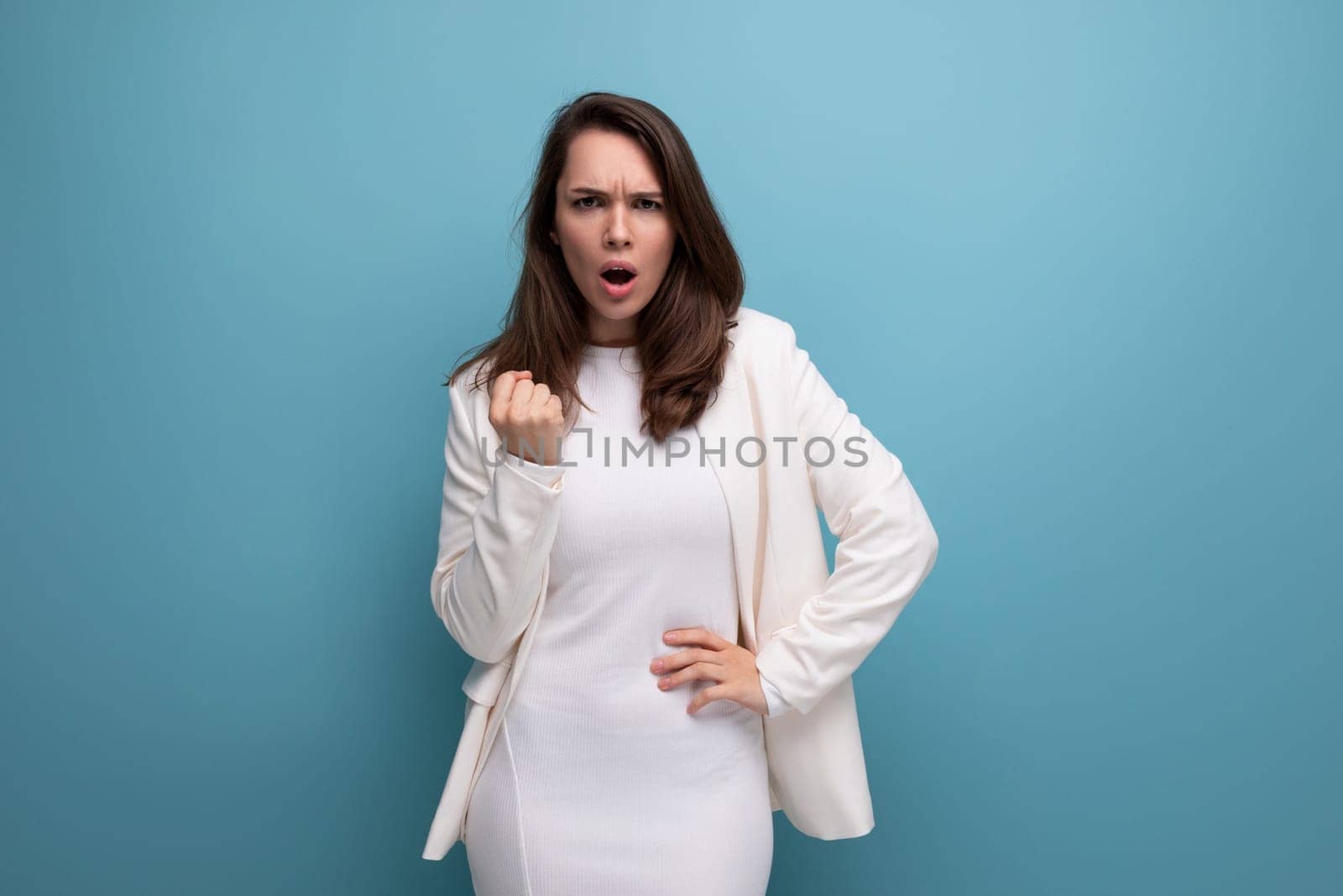 caucasian brunette woman in an ivory jacket and a white dress shows with her hand for some idea.