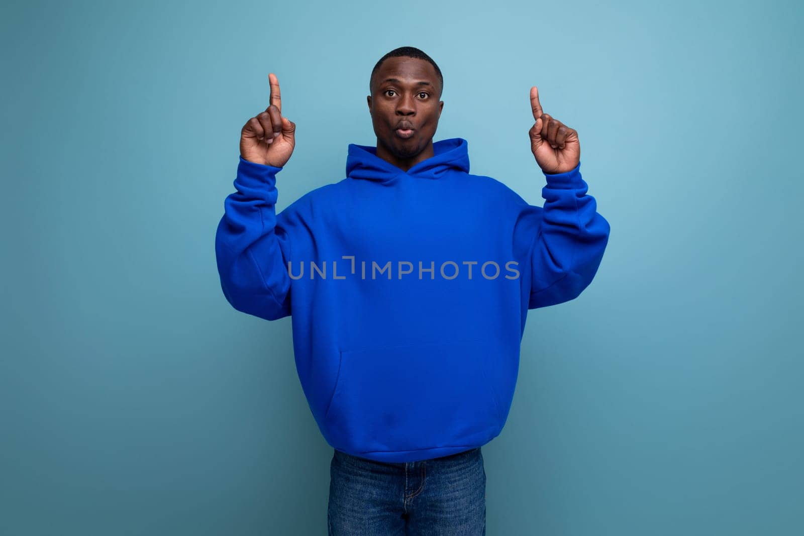 a young african guy in a stylish hoodie demonstrates with his hand on an advertisement on a studio background with copy space.