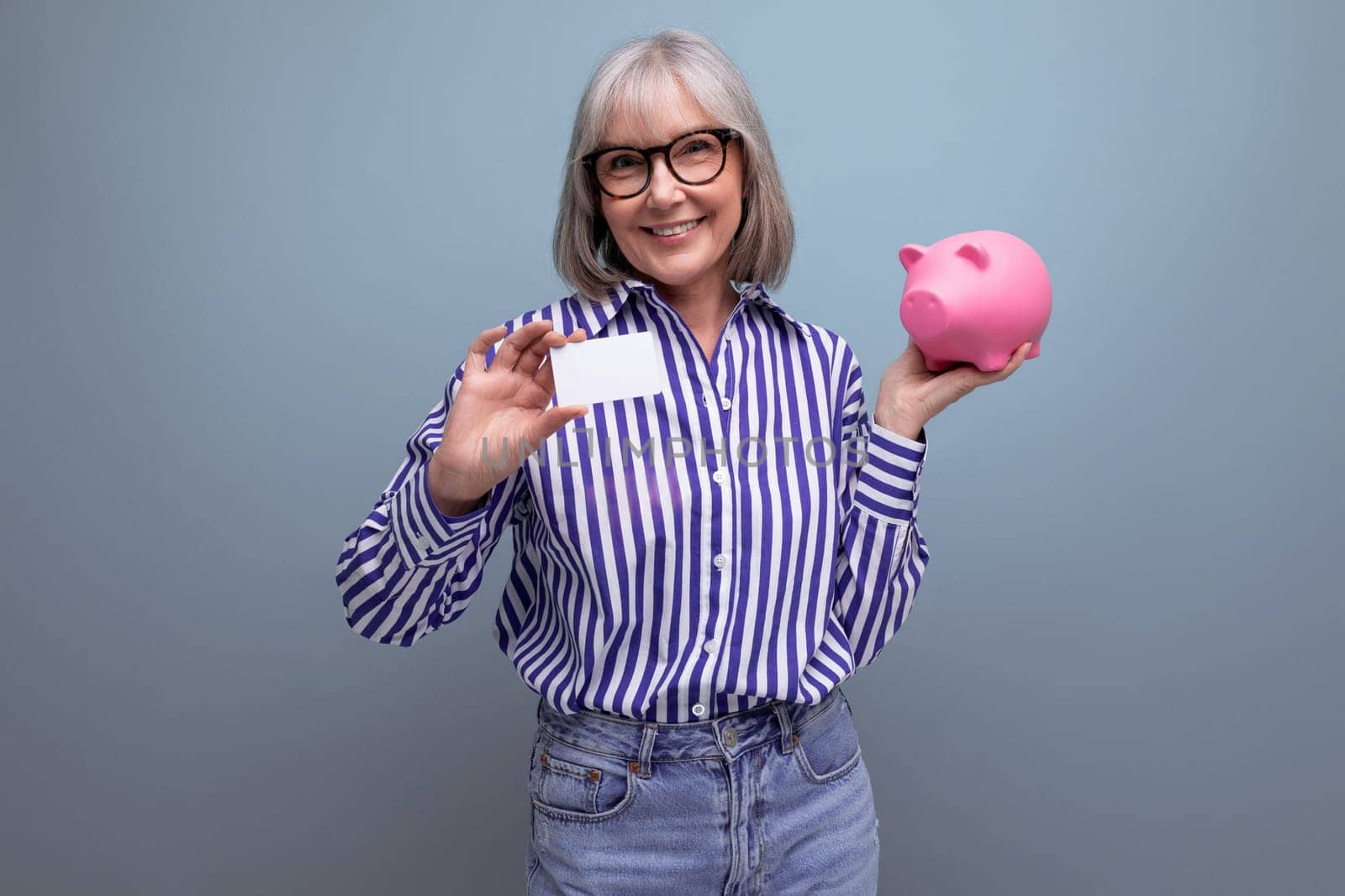 middle-aged woman with gray hair holding a piggy bank and a credit card with a mocap on a bright studio background.