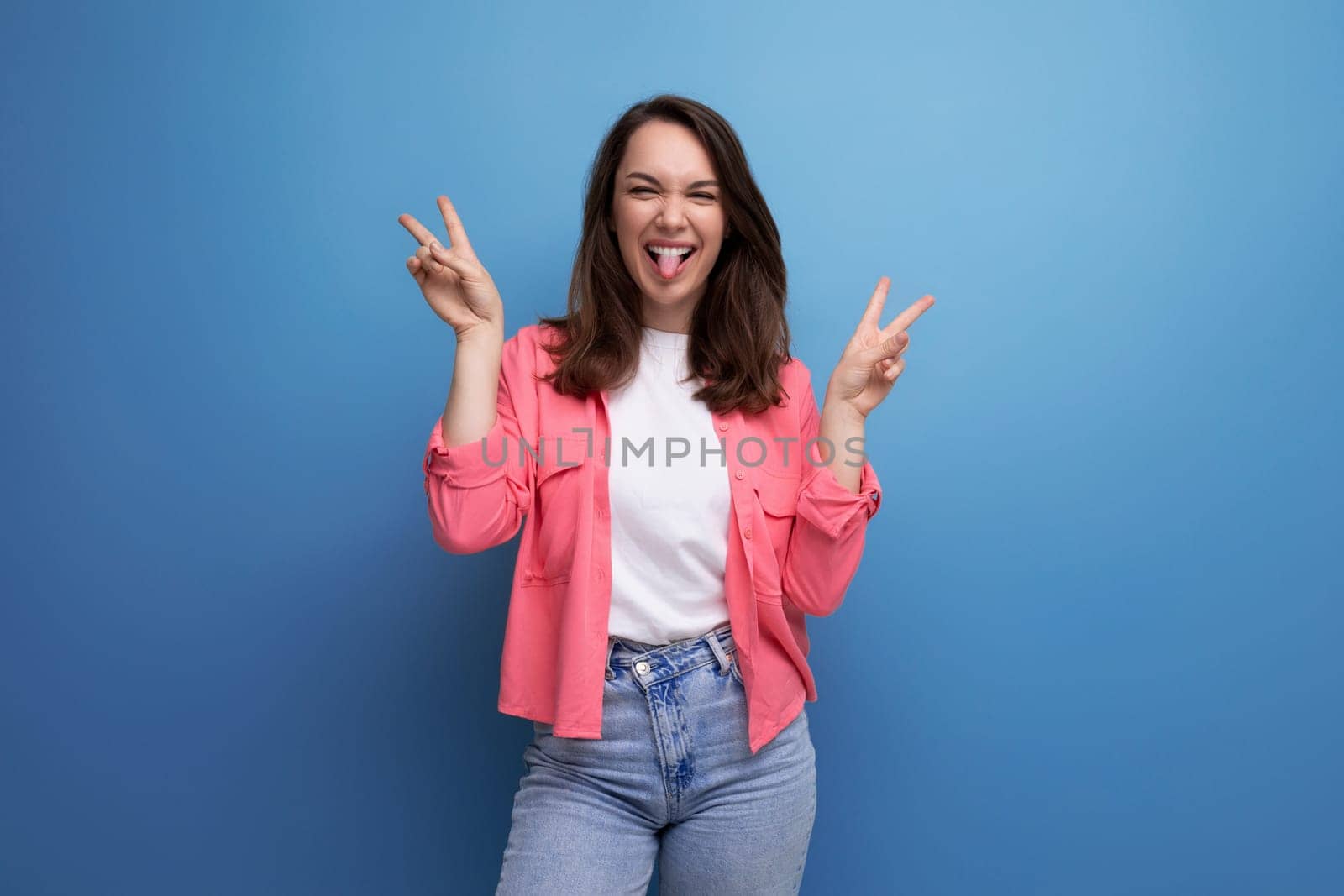 positive brunette young woman in pink shirt and jeans on studio isolated background.