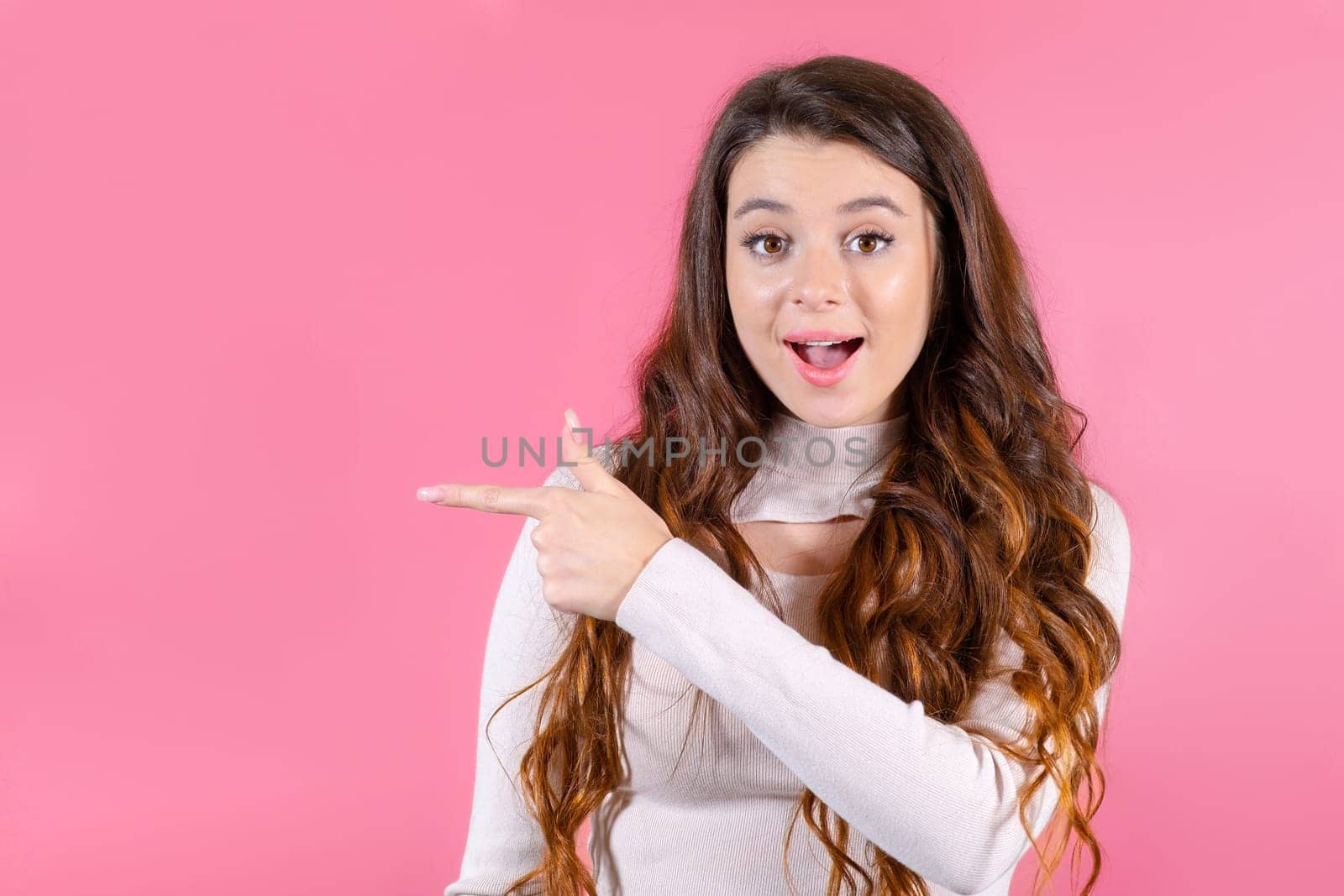 A young lady's smile shines and her finger pointing to the copy space on the pink background.