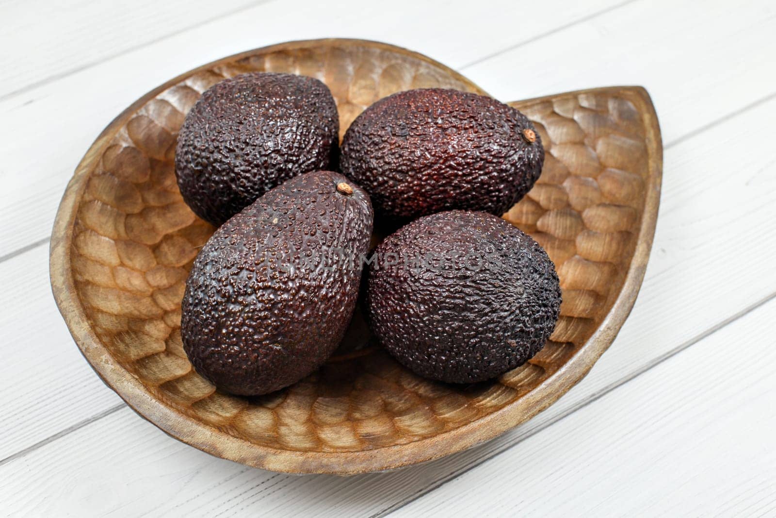 Dark brown avocados ( bilse variety ) on wooden carved bowl.