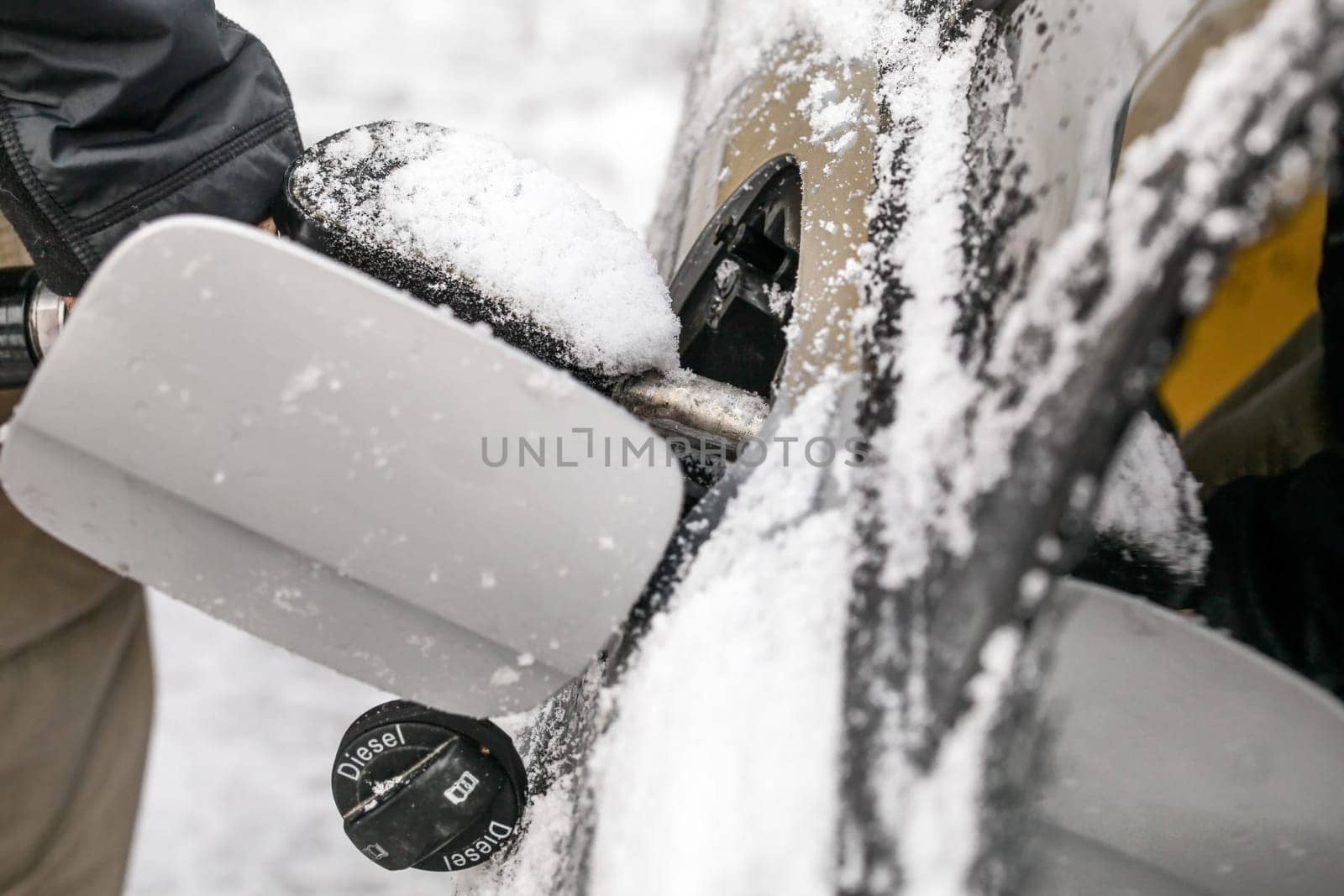 Detail on man refuelling his diesel car in winter, gas tank door covered with snow.