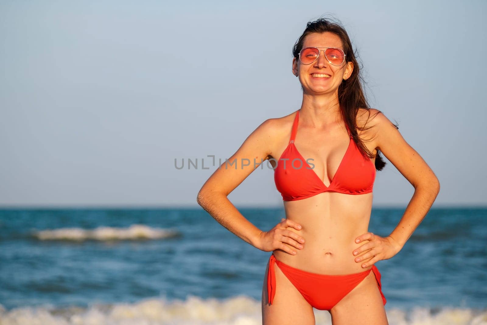 Woman in bikini. Young woman in red bikini on beach looking at camera. Beautiful girl in swimwear with copy space. Summer vacation and tanning concept. download photo