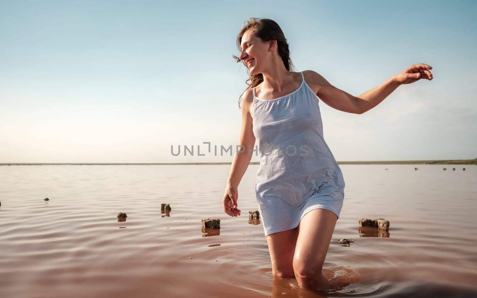 Young woman walking in red lake. Happy girl in striped white dress smiling and looking away. Sexy fashion woman enjoys summer holidays. download photo