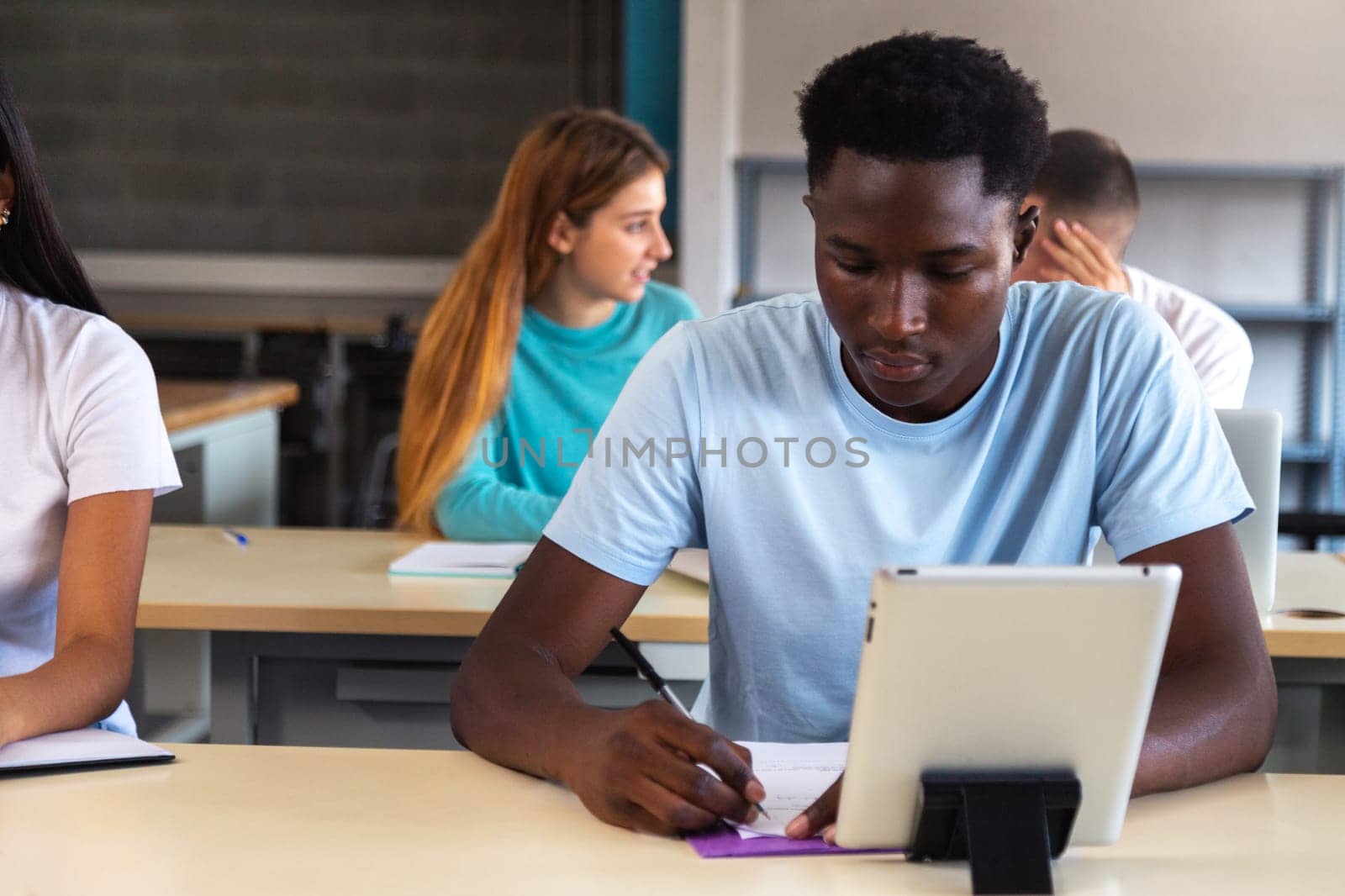 Teen black male student using digital tablet in class. African American high school male student doing homework. Copy space. Education concept.
