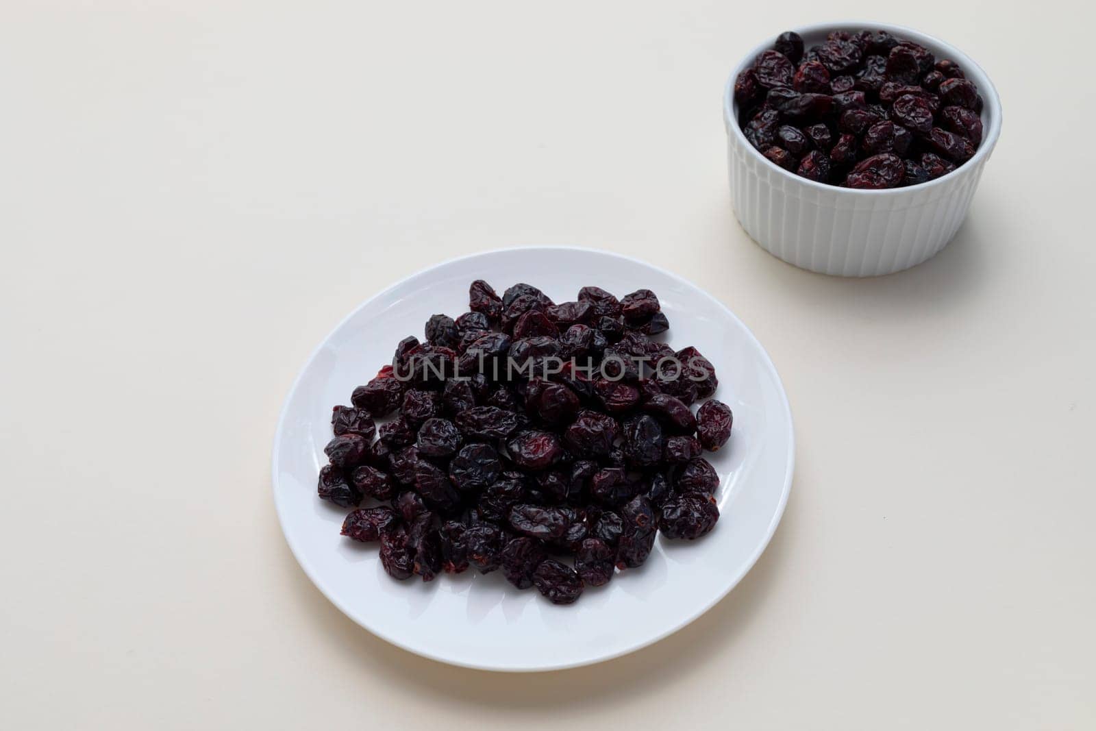 Dried Cranberries On White Plate On Beige Background. Superfood. Selective Focus. Sweet Dehydrated Cranberries. Nutrients And Vitamins. Horizontal Plane. High quality photo
