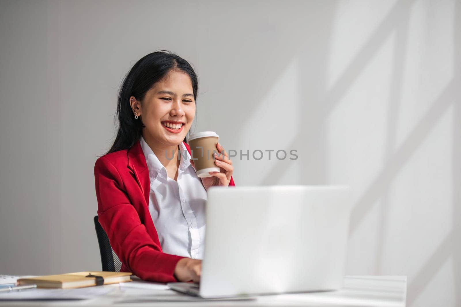 Cheerful business lady working on laptop in office, Asian happy beautiful businesswoman in formal suit work in workplace. Attractive female employee office worker smile. by wichayada