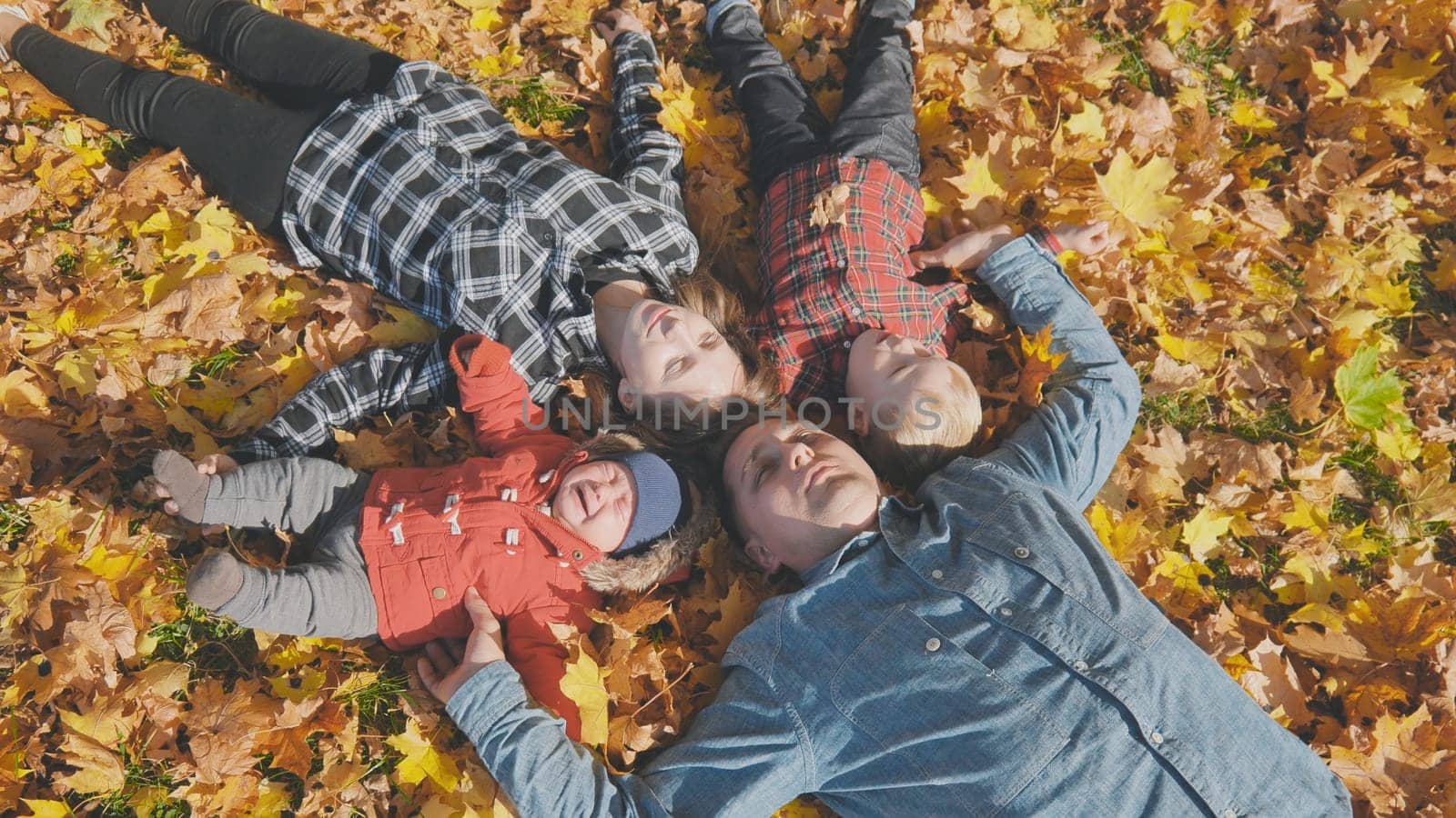 The happy family lies on their backs in the autumn leaves