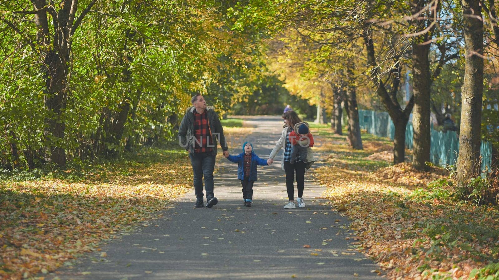 A happy young family walks along a city park road in the fall