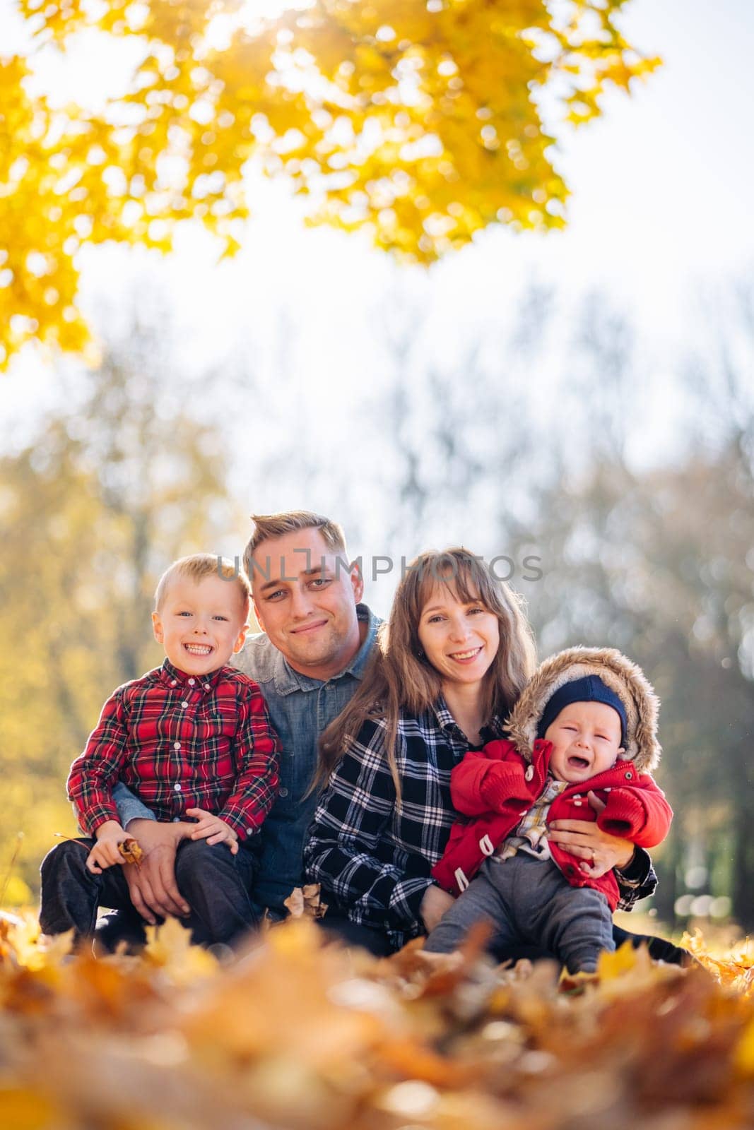 A young family sits in the park on a leafy, sunny autumn day