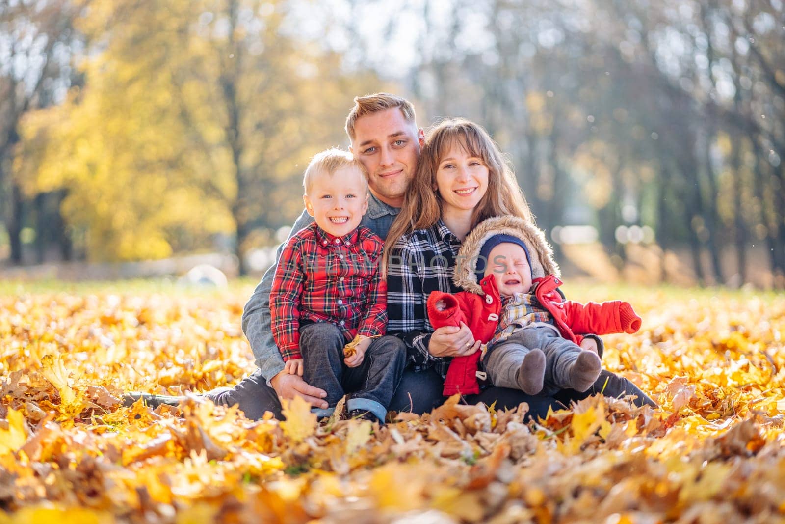 A young family sits in the park on a leafy, sunny autumn day