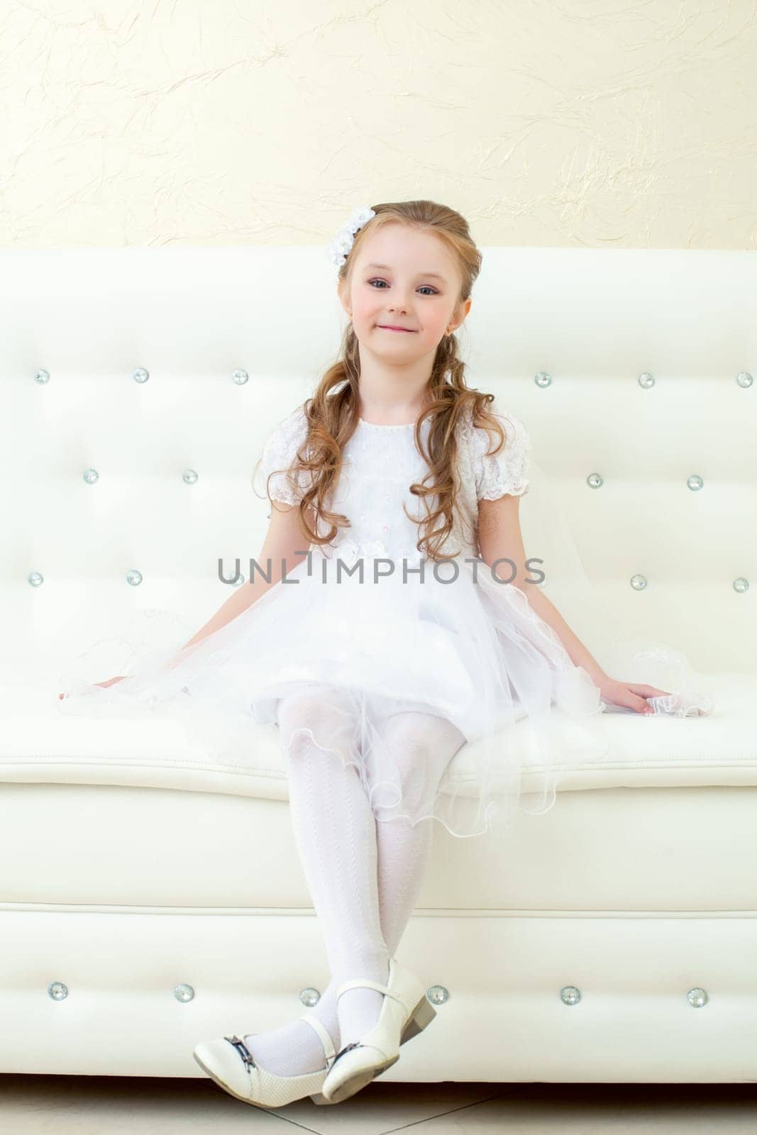 Funny little girl posing sitting on white sofa, close-up