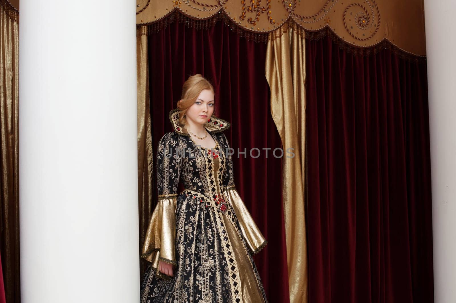 Young actress in royal dress posing on curtain backdrop