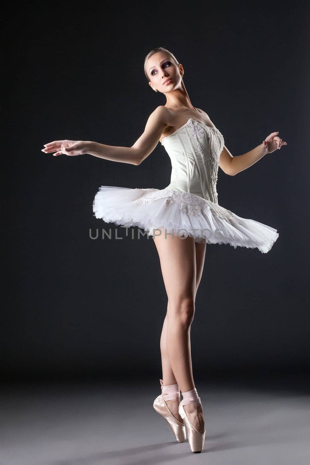 Image of cute young ballerina dancing in studio, on gray background
