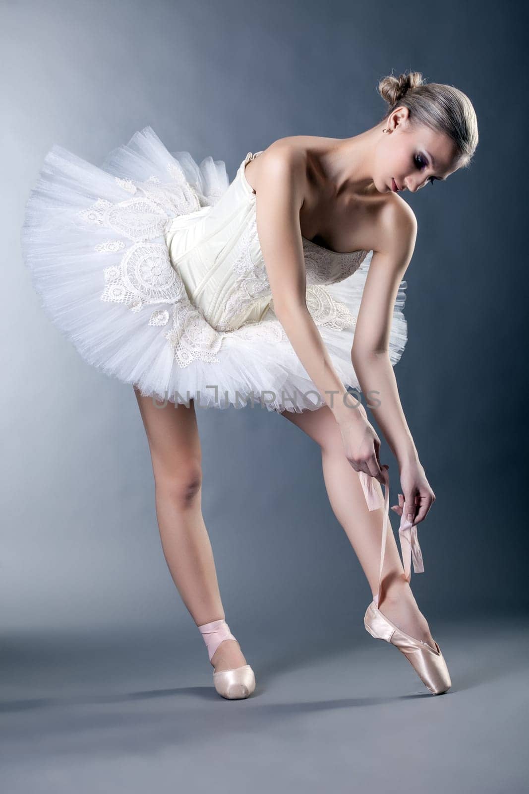 Image of beautiful young ballerina tying pointe in studio