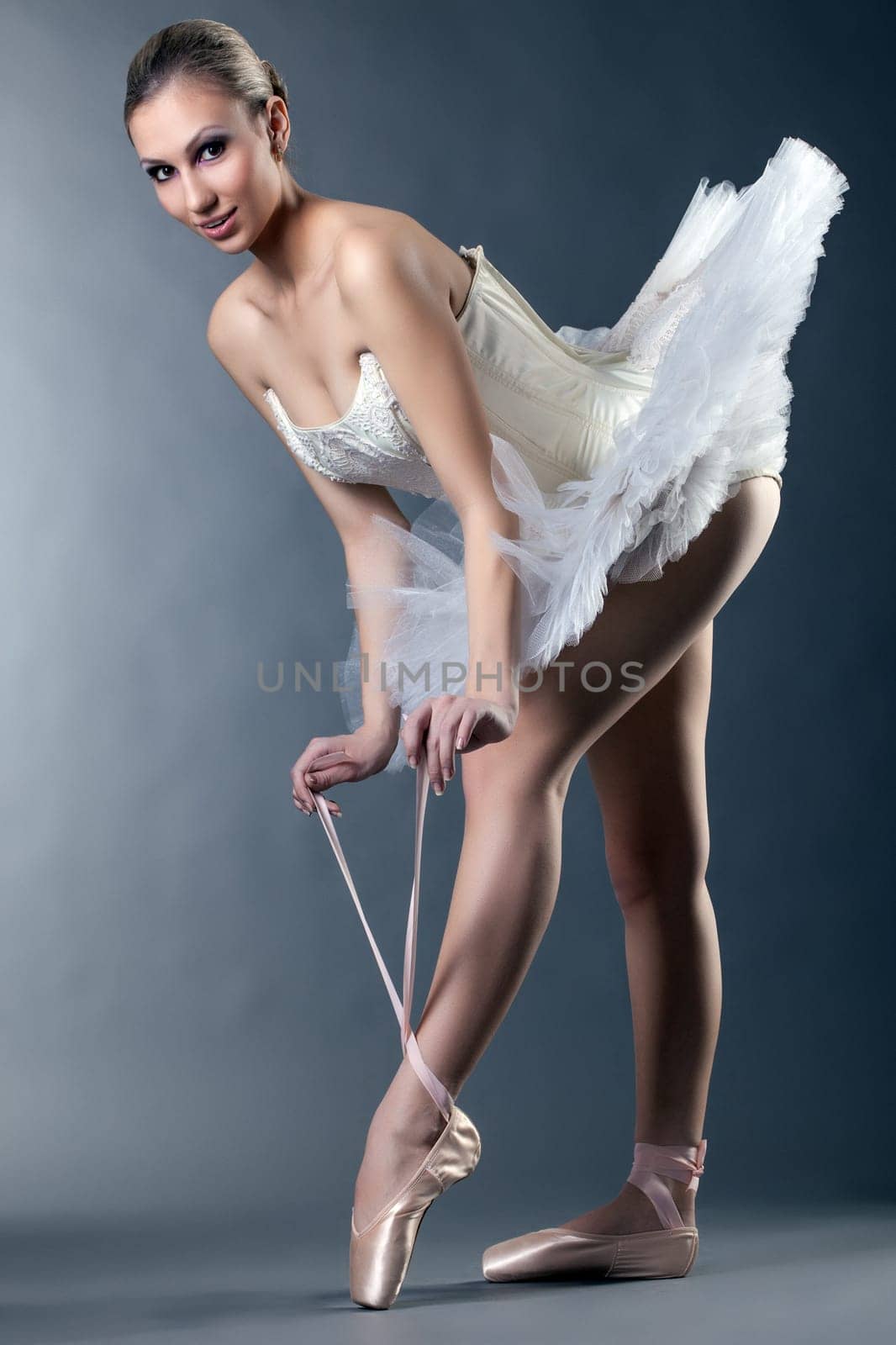 Charming female ballet dancer posing tying pointe in studio