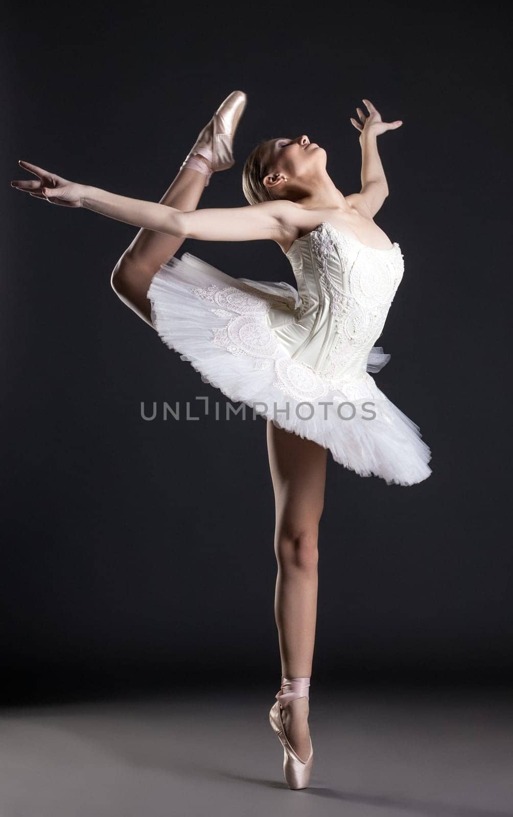 Image of flexible cute ballerina dancing in studio, on gray background