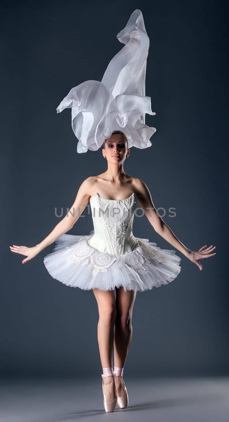 Lovely young ballet dancer posing in studio, on gray background