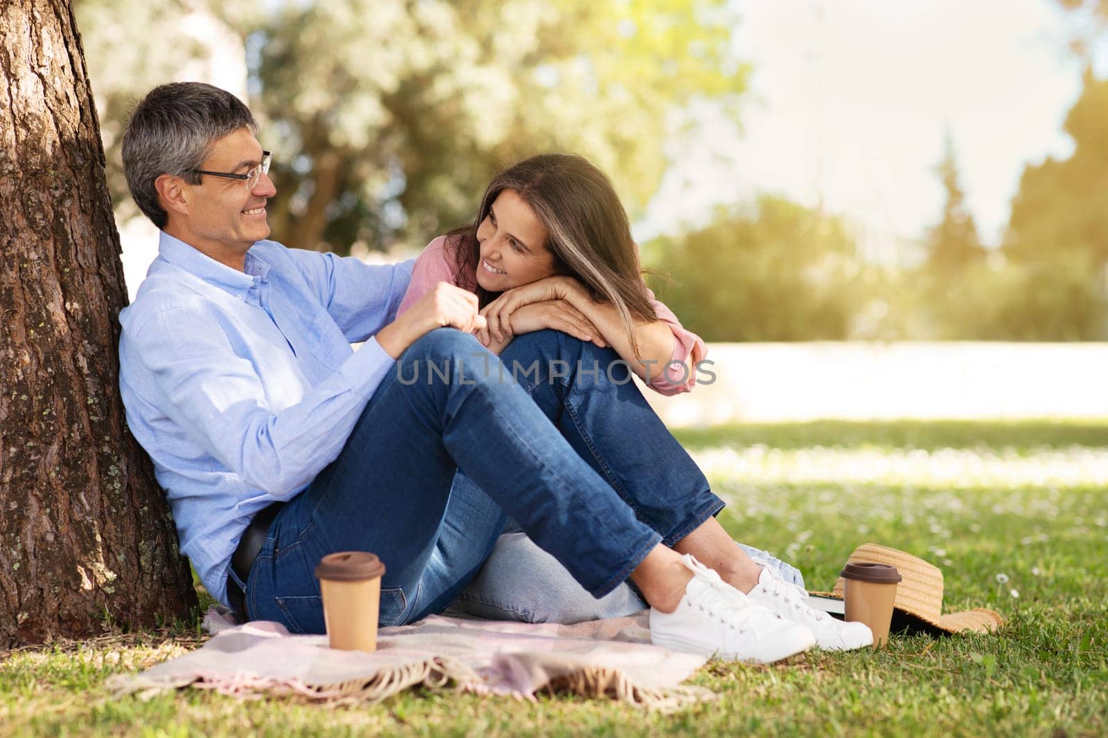 Loving Mature Couple Relaxing Together Outdoors In Summer Park, Happy Romantic Middle Aged Spouses Sitting On Plaid Under Tree And Drinking Takeaway Coffee, Enjoying Picnic Outside, Copy Space