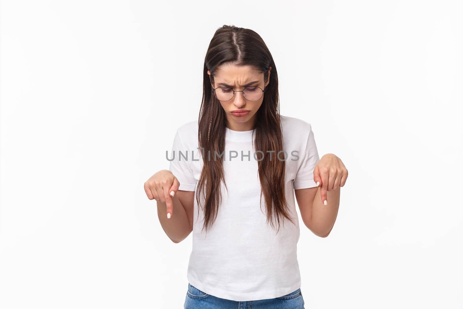 Waist-up portrait of unsure, skeptical young brunette female in glasses and t-shirt, look perplexed, cant figure out what is this lying down, pointing and looking bottom advertisement puzzled by Benzoix