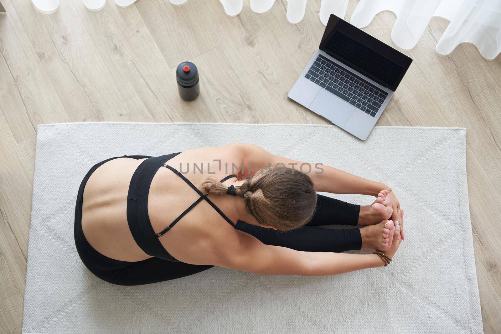 Yoga paschimottanasana forward bend pose by young woman. Young yogi practice yoga poses relaxing in studio with laptop