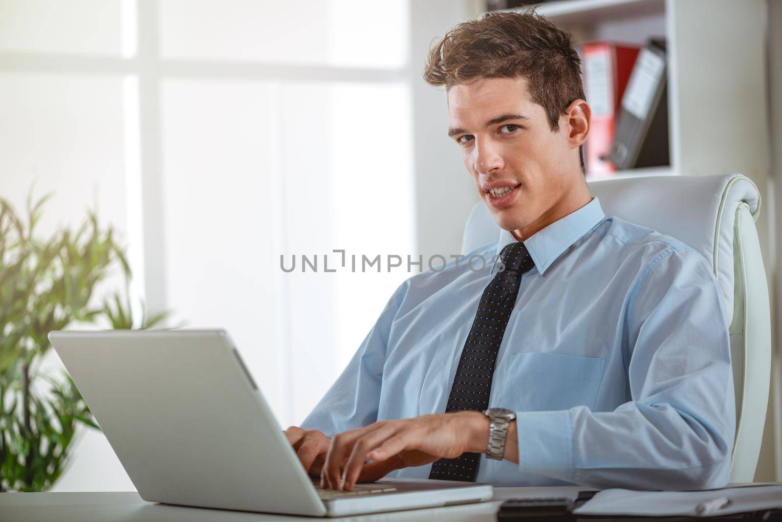 Executive satisfied male working at laptop looking at documents and accounts. He is typing and looking concentrated and serious.