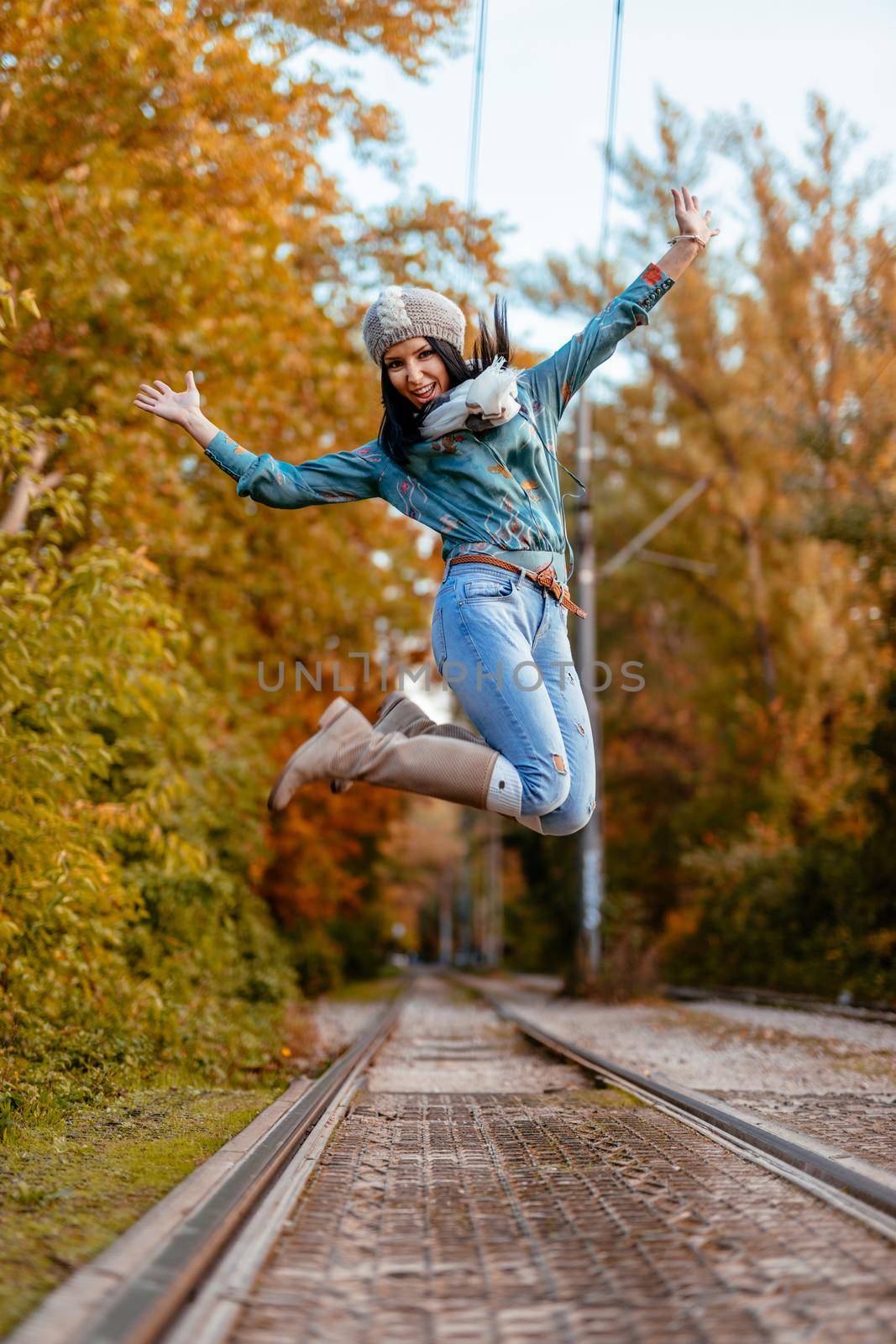 Beautiful young cheerful woman enjoying in autumn colors jumping in the city park with happyness.