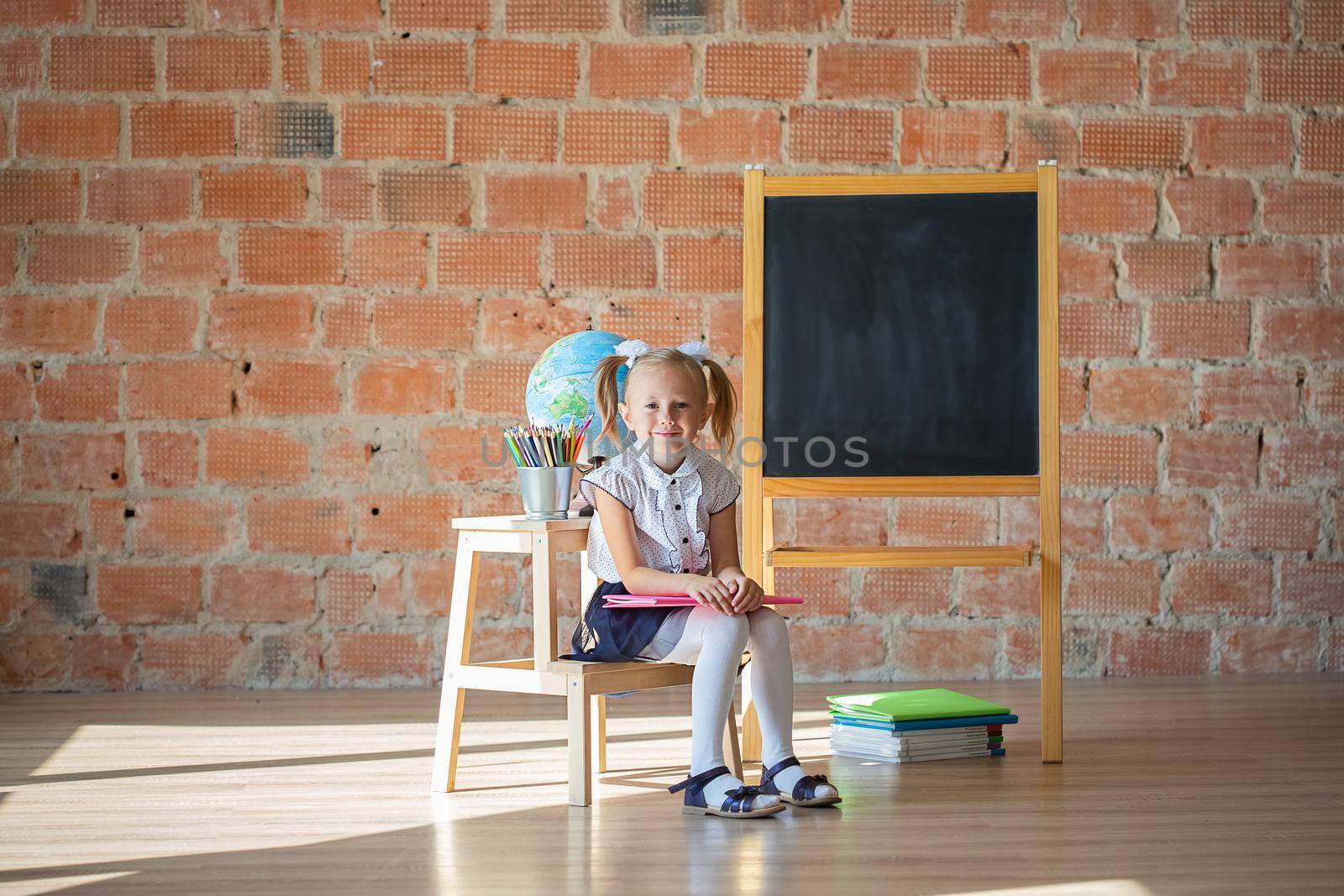Portrait of caucasian school kindergarten girl sitting in front of blackboard with a book, back to school concept