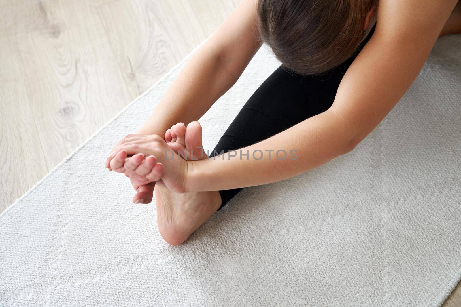 Top view of young woman practicing yoga, sitting in Seated forward bend exercise, paschimottanasana pose, working out, wearing sportswear by Mariakray