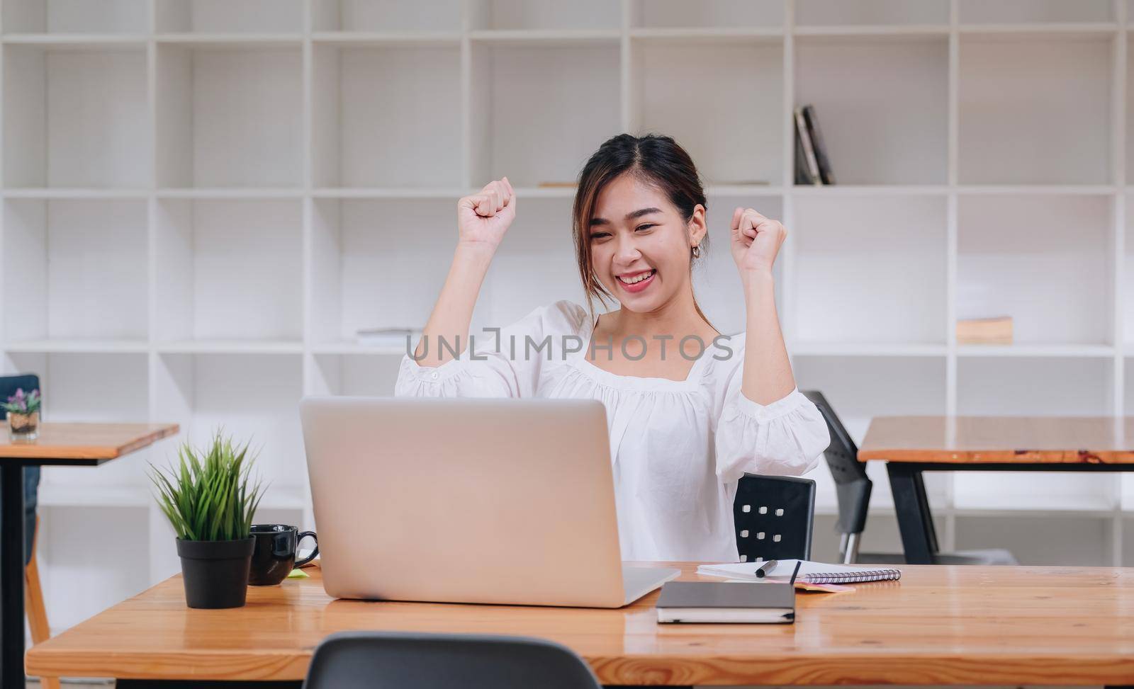 Happy excited asian woman at home workstation triumphing with raised hands, female using laptop computer with online meeting by nateemee