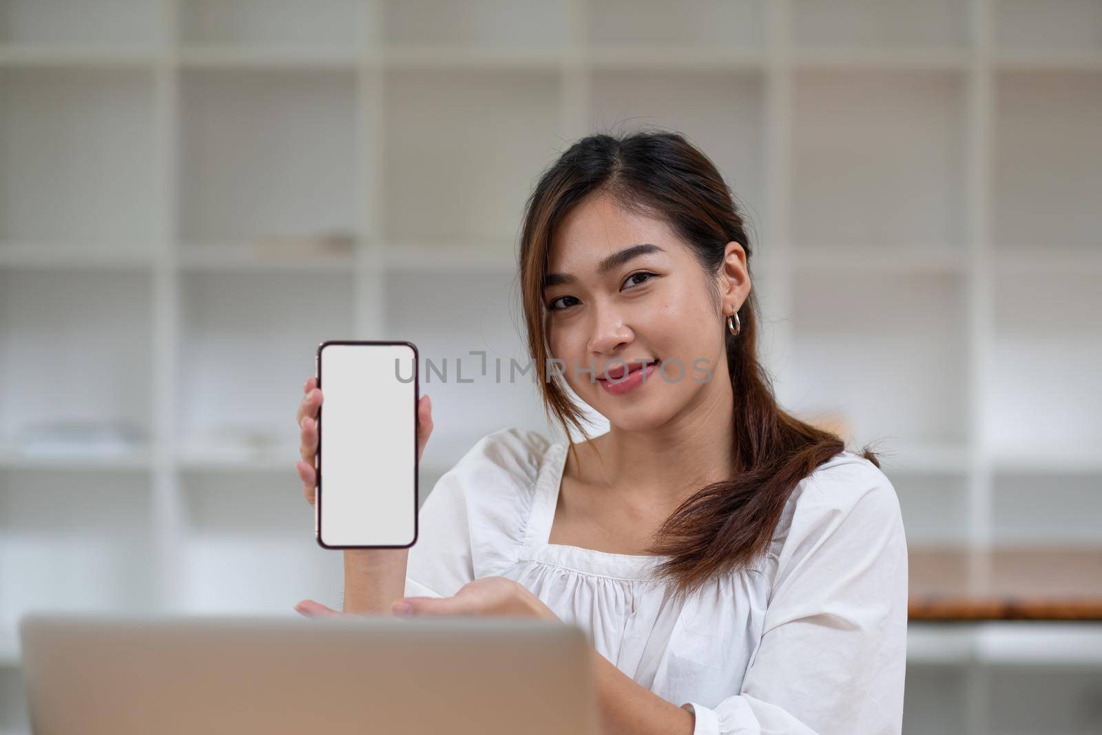 Portrait of attractive cheerful asian woman demonstrating device gadget with white screen for text advertising.