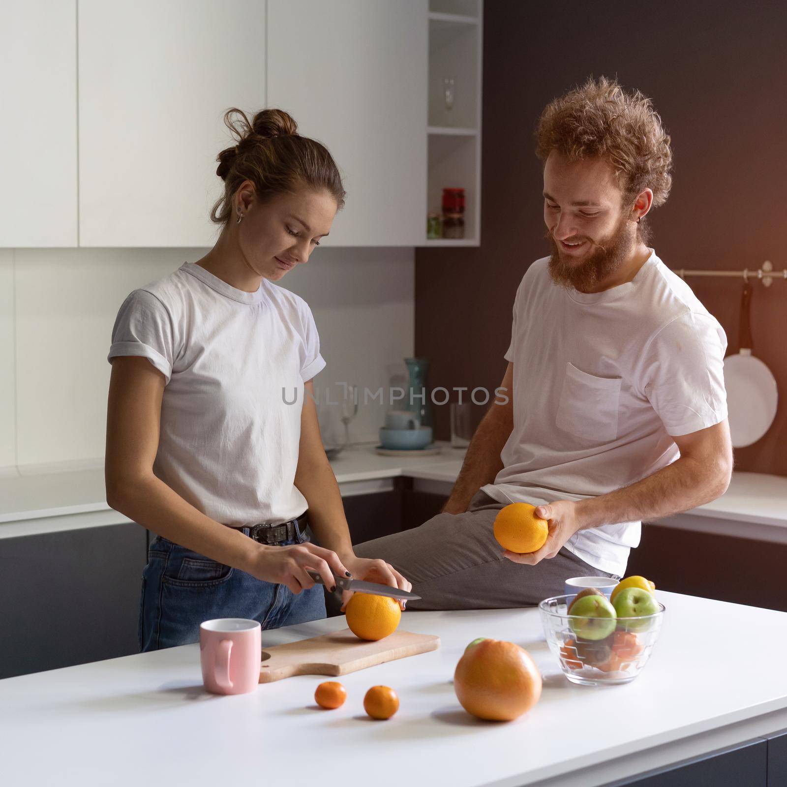 Couple making fun cooking together at modern kitchen in a new house. Beautiful young couple happy of their new home. Pretty girl feeds or nursing her boyfriend. New house concept. Square cropped.