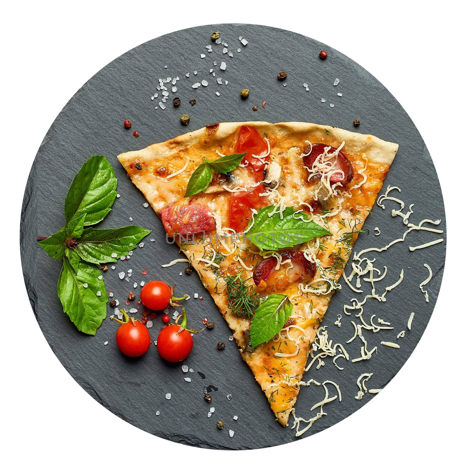 Delicious triangular slice of pizza with smoked sausages, mushrooms, tomatoes, cheese and basil leaves on a black graphite board, top view