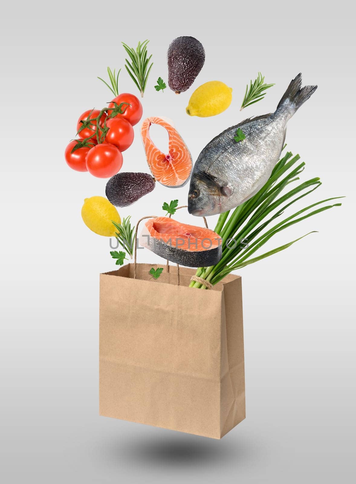 Brown kraft bag and levitating pieces of salmon, lemon, avocado, and onion sprouts on a gray background. Concept of healthy food shopping