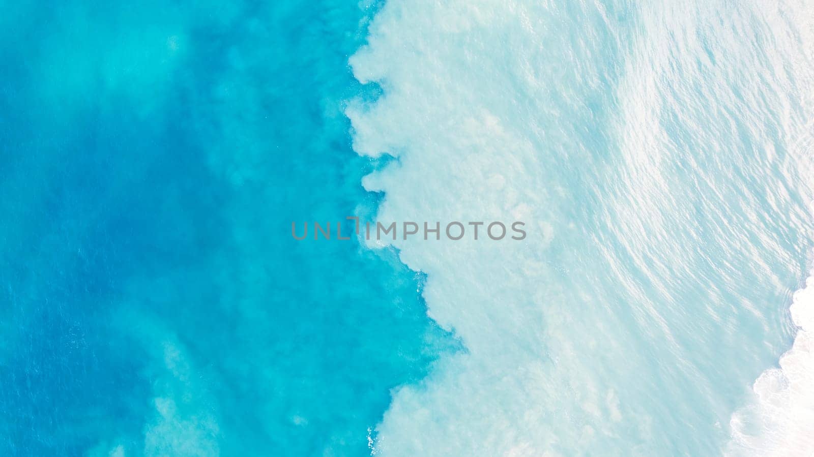 Top view of light blue water with white sand. Waves raise sand and a mix with turquoise water is obtained. Shadows from clouds on a clear ocean. Clear sea. Gradient of blue. The background photo
