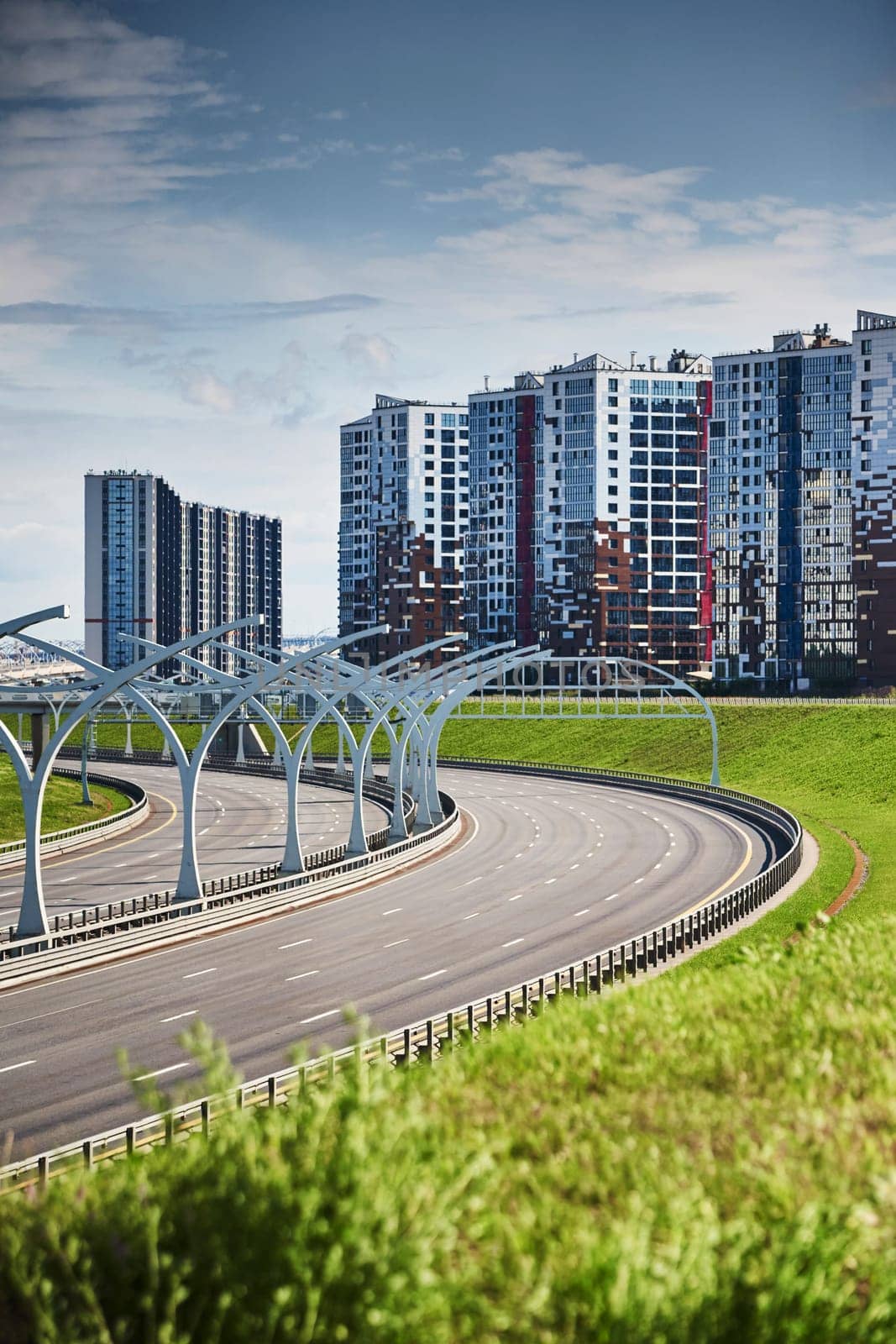 Empty expressway of the western high-speed diameter in st. petersburg in clear sunny weather, green lawns along the road, new residential buildings stand on a hillock, lamppost, colourful facade. High quality photo