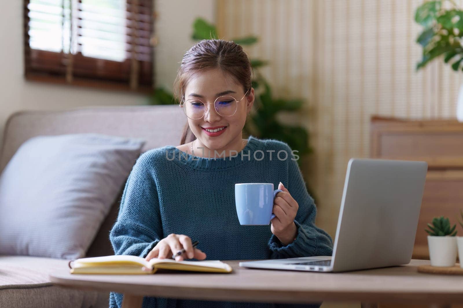 Young asian relaxed smiling pretty woman relaxing with laptop at home. Female feeling joy enjoying with mobile phone on cozy couch by itchaznong