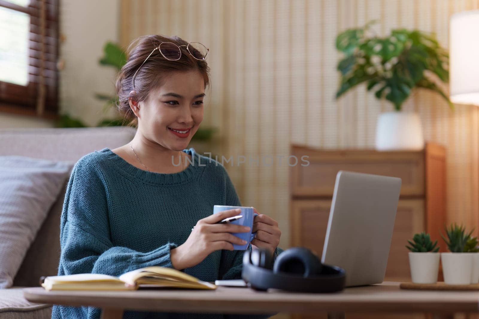 Young asian relaxed smiling pretty woman relaxing with laptop at home. Female feeling joy enjoying with mobile phone on cozy couch.