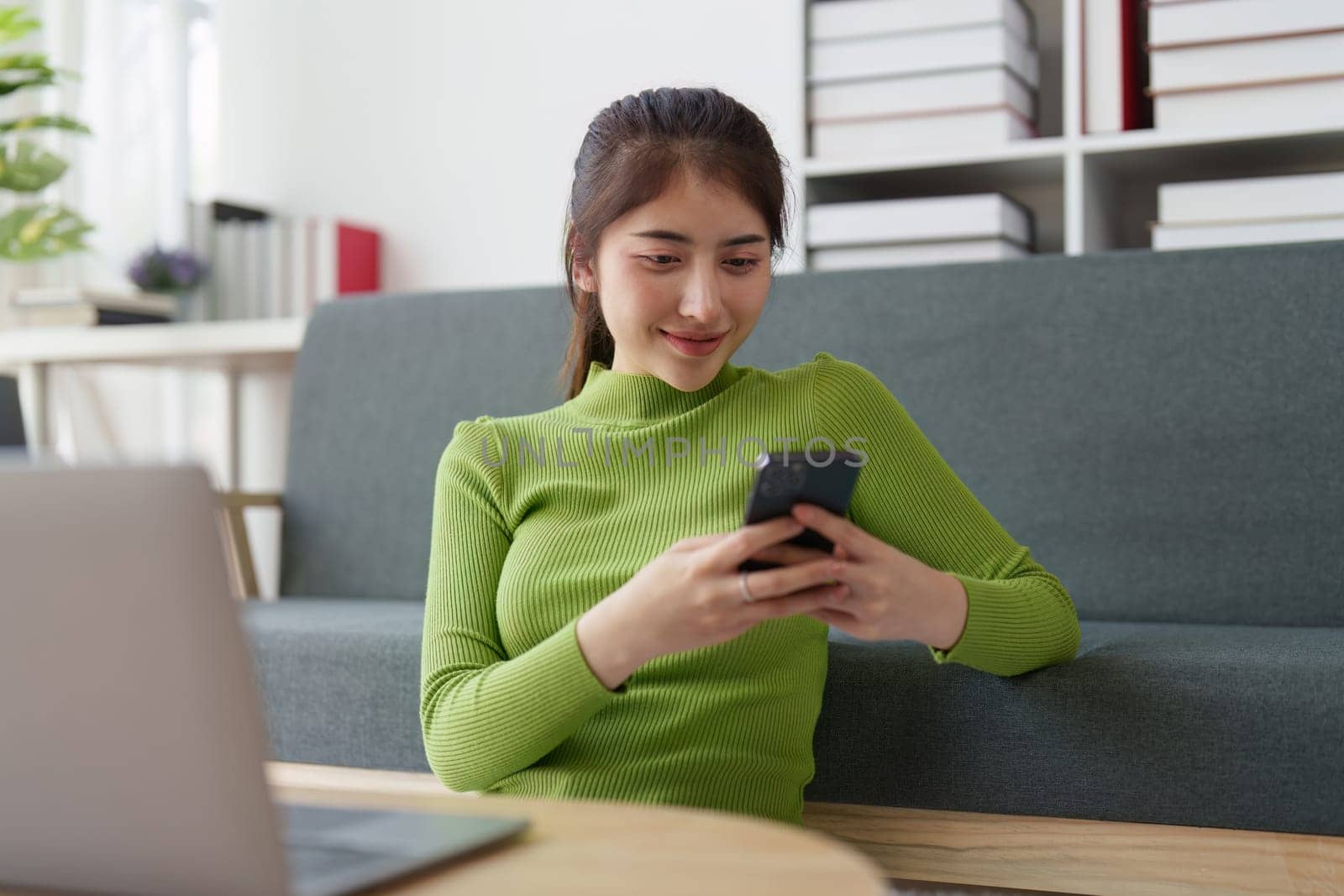Young asian relaxed smiling pretty woman relaxing with mobile phone at home. Female feeling joy enjoying with mobile phone on cozy couch.