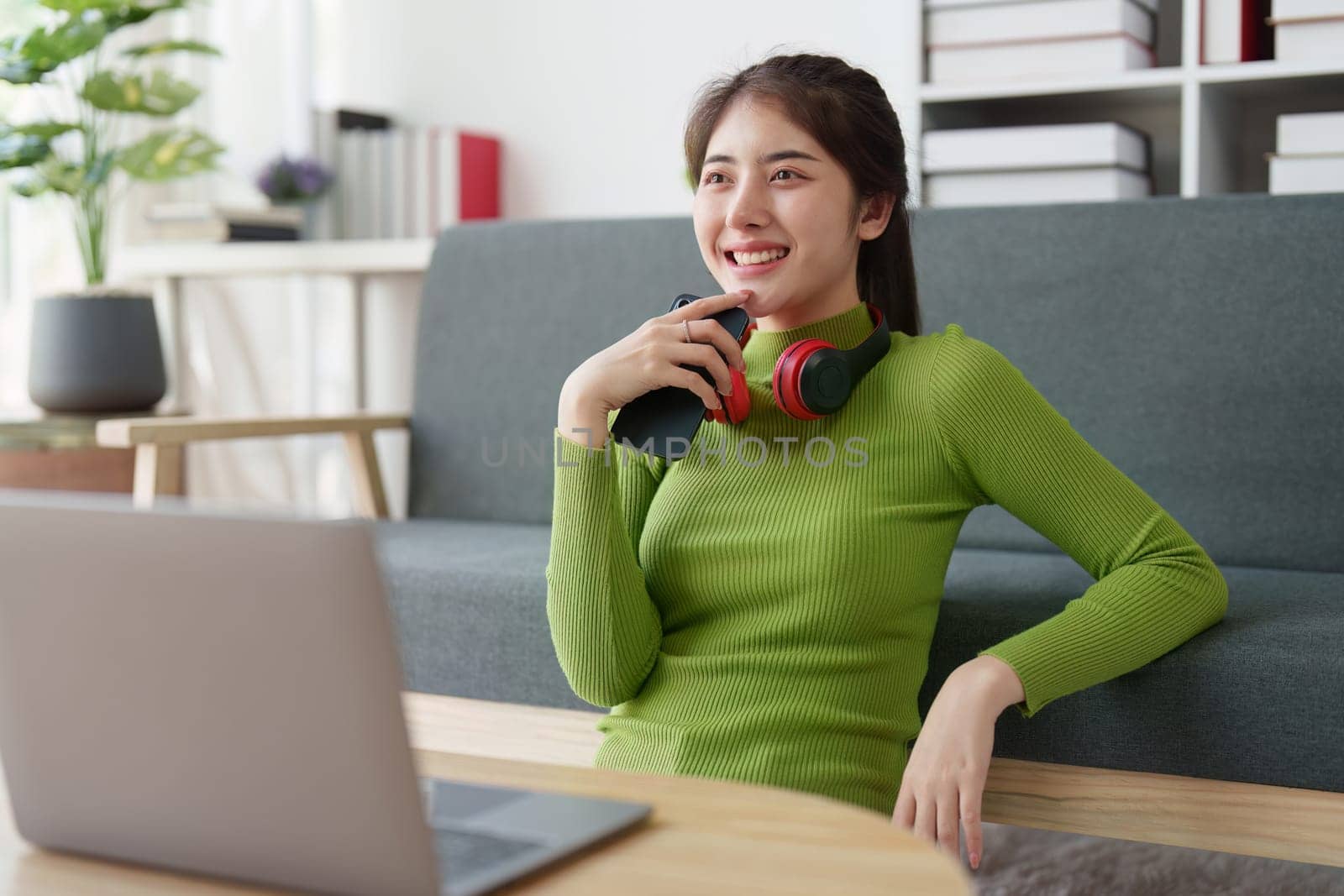 Young asian relaxed smiling pretty woman relaxing with mobile phone at home. Female feeling joy enjoying with mobile phone on cozy couch.