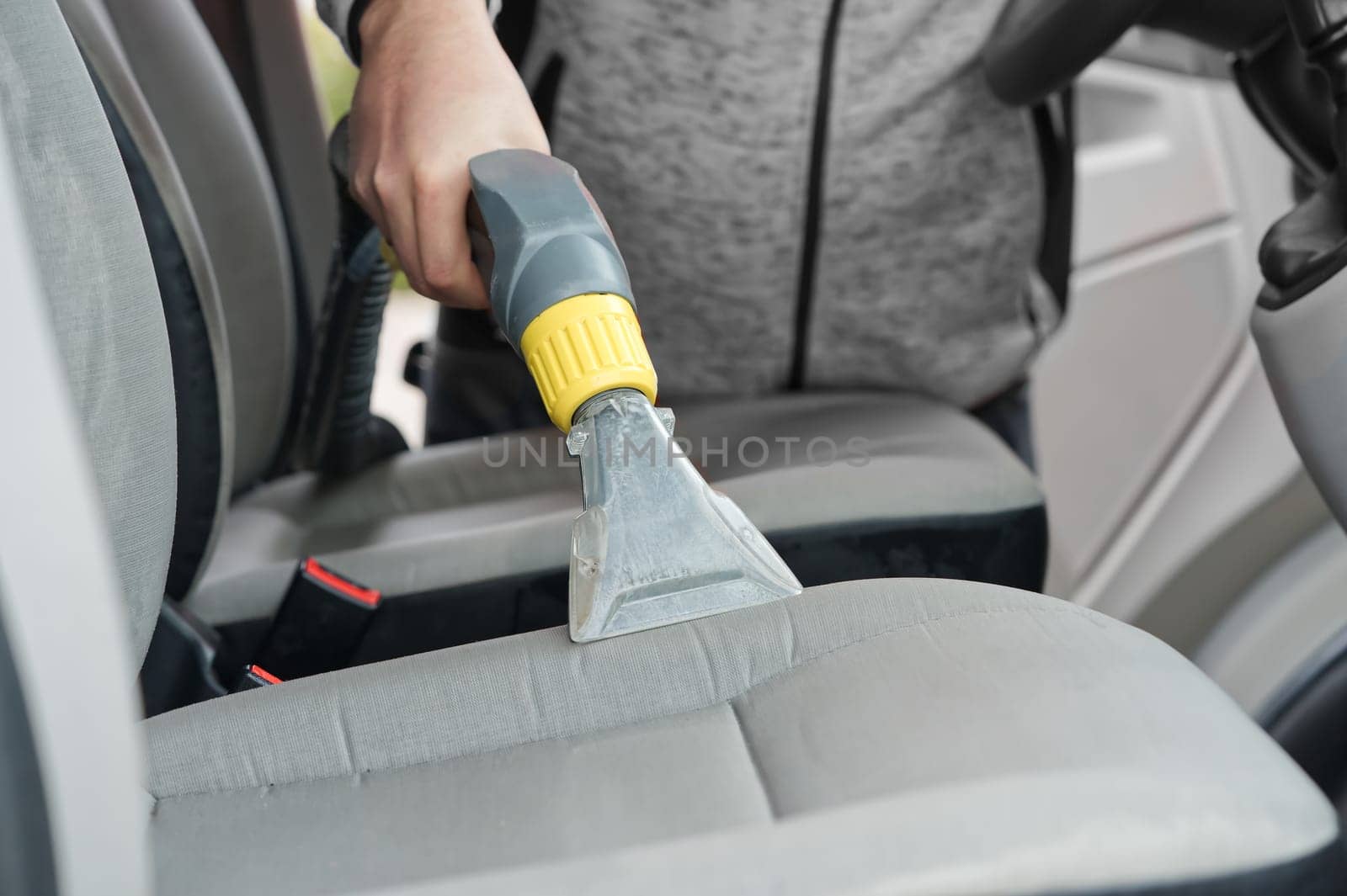 Handyman vacuuming car front textile seat with vacuum cleaner. man cleaning work machine by PhotoTime