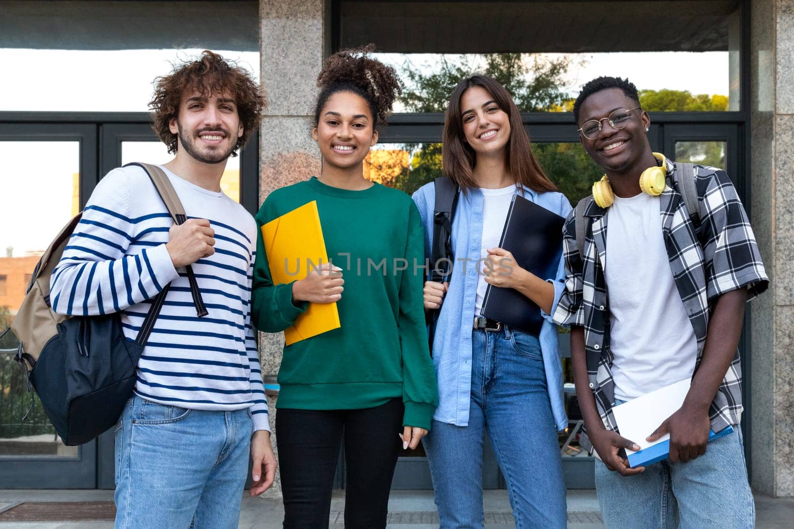 Group of happy and smiling multiracial college students standing in front of university building looking at camera. Education concept.