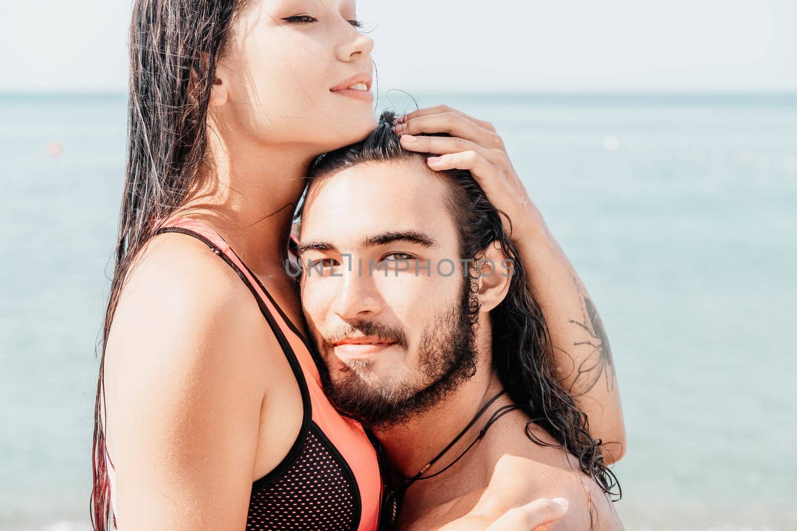 Close up shot of beautiful young caucasian woman with black hair and freckles looking at camera and smiling. Cute woman portrait in a pink bikini posing on a volcanic rock high above the sea