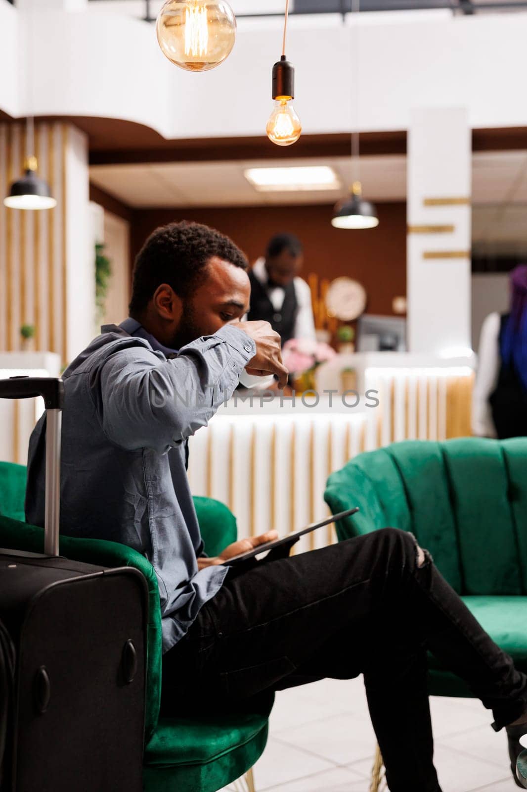 African American businessman drinking coffee and resting while waiting for check-in hotel lobby, black guy tourist holding digital tablet checking in online. Travel, vacation and business trip