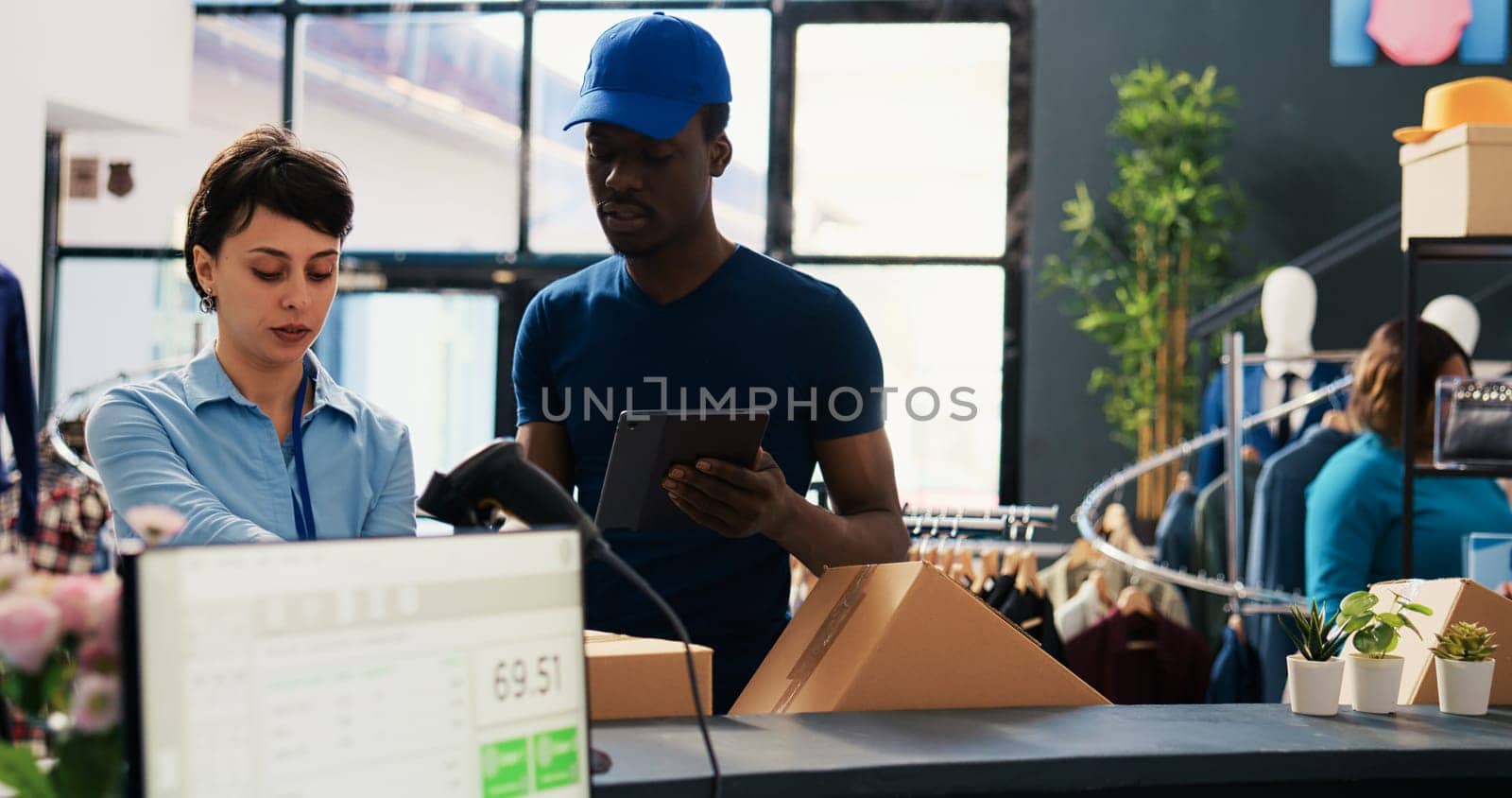 African american courier explaining orders distribution report to store manager in modern boutique. Employee putting fashionable clothes in boxes, preparing packages for delivery in shopping mall