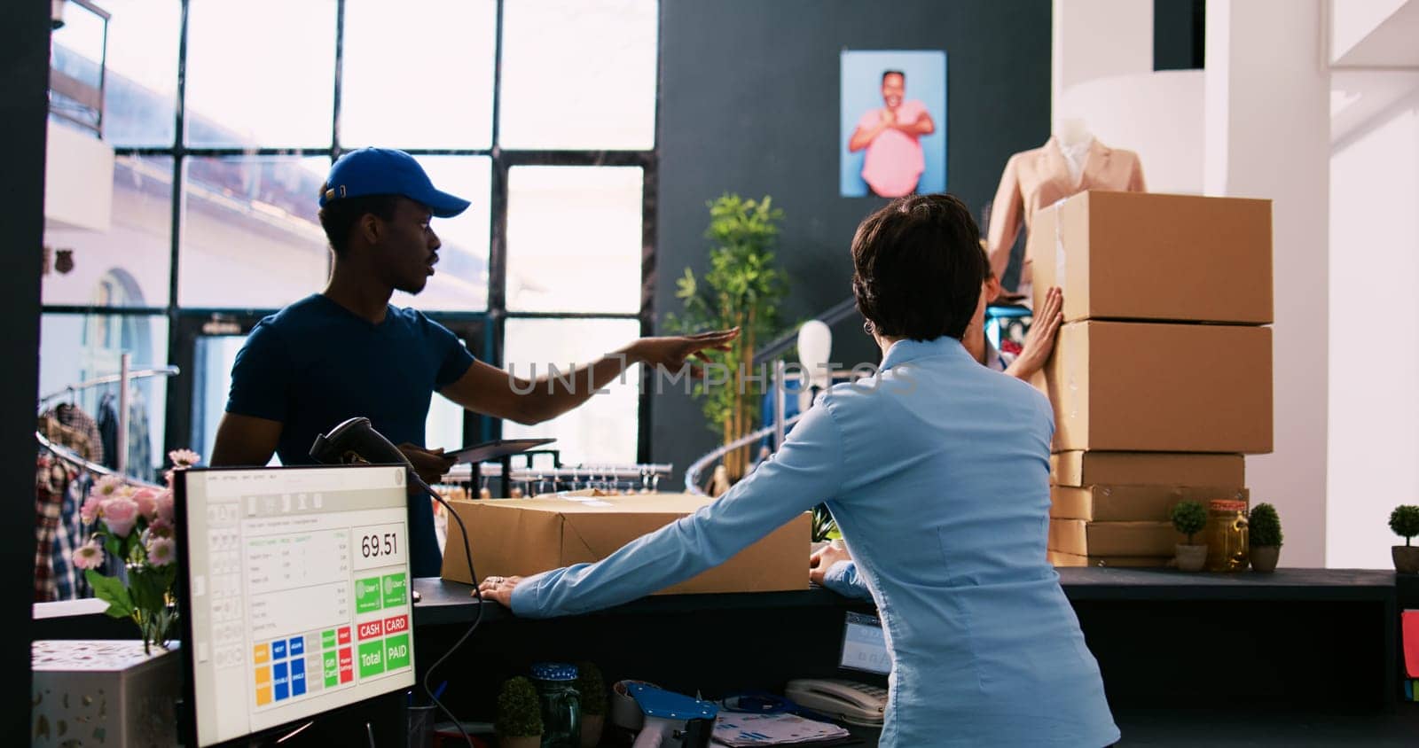 African american deliveryman showing packaging report to worker, discussing online orders details in clothing store. Employee standing at counter desk, preparing packages for delivery in shopping mall