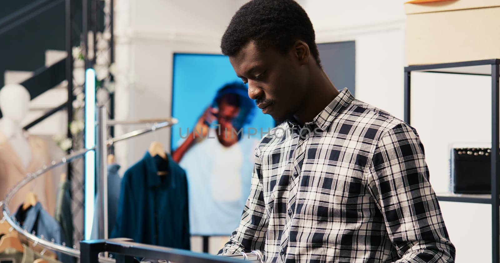African american man shopper looking at new fashion collection, analyzing merchandise fabric in modern boutique. Shopaholic customer shopping for fashionable clothes in clothing store